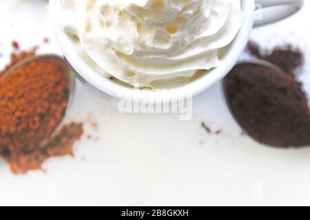 Tasse Cappuccino mit Zimt und verschütteten Kaffeebohnen. Eine Tasse Kaffee mit Schlagsahne auf dem Hintergrund verschiedener Kaffee und Gewürze. Stockfoto