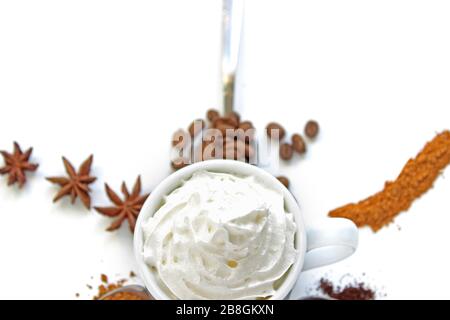 Tasse Cappuccino mit Zimt und verschütteten Kaffeebohnen. Eine Tasse Kaffee mit Schlagsahne auf dem Hintergrund verschiedener Kaffee und Gewürze. Stockfoto