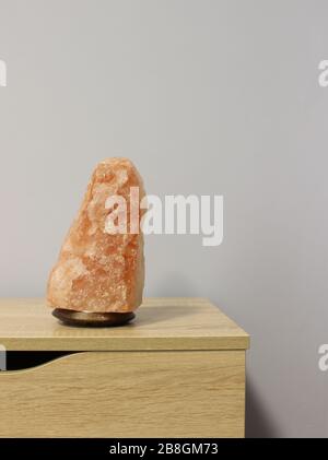 Ausgeschaltet wurde eine rosafarbene Salzlampe aus dem Himalaya, die in Form eines Felsens auf einem hellen Tisch gehauen wurde. Stockfoto