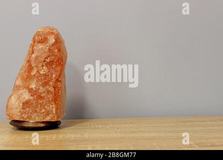 Ausgeschaltet wurde eine rosafarbene Salzlampe aus dem Himalaya, die in Form eines Felsens auf einem hellen Tisch gehauen wurde. Stockfoto