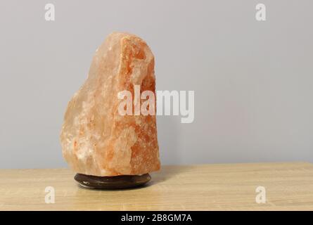 Ausgeschaltet wurde eine rosafarbene Salzlampe aus dem Himalaya, die in Form eines Felsens auf einem hellen Tisch gehauen wurde. Stockfoto