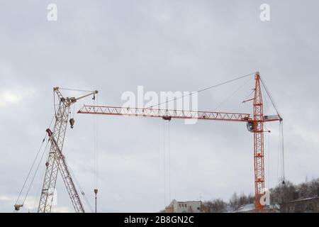 Mehrere Baukräne arbeiten an einer Baustelle. Silhouetten gegen den weißen Himmel. Stockfoto