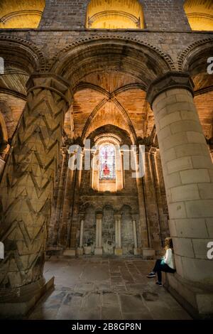 Weibliche Touristin sitzt auf der Basis einer geschnitzten Säule, die die Glasmalerei in Dunfermline Abbey, einer Church of Scotland Parish Church, Dunfermline, bewundert; Stockfoto