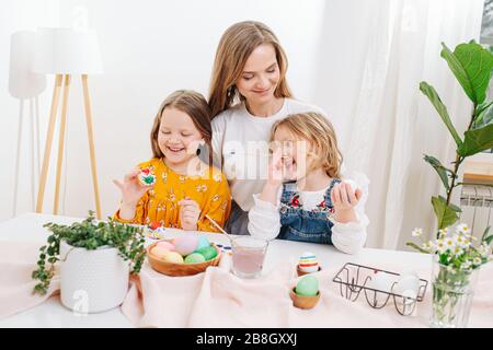 Mutter verbrachte Zeit mit ihren beiden Töchtern und malte ostereier hinter einem Tisch Stockfoto