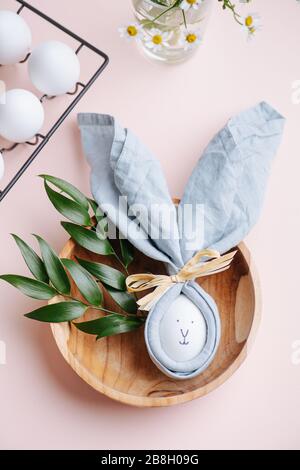 Osterei in Serviette mit einem darauf gemalten Kaninchengesicht in einer Holzschale. Stockfoto