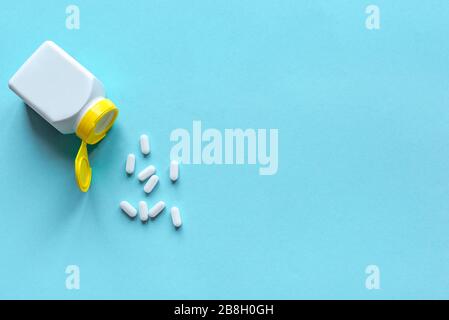 Tablettenflasche und Pillen auf blauem Hintergrund, Draufsicht, Kopierraum. Medizin- und Apothekenkonzept. Vitamine oder generische Tabletten. Stockfoto