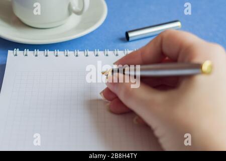Weiblicher Handhalter mit leeren Noten und einer Tasse Kaffee auf blauem Hintergrund, selektiver Fokus Stockfoto