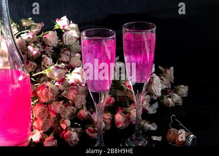 Strahlend brillantes Himbeer-Getränk. Sekt in zwei Gläsern steht auf einem Holztisch mit Eis. Für Blumen und eine Girlande. Kopierbereich Stockfoto