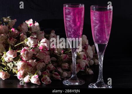 Strahlend brillantes Himbeer-Getränk. Sekt in zwei Gläsern steht auf einem Holztisch mit Eis. Für Blumen und eine Girlande. Kopierbereich Stockfoto