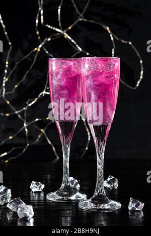 Strahlend brillantes Himbeer-Getränk. Sekt in zwei Gläsern steht auf einem Holztisch mit Eis. Für Blumen und eine Girlande. Kopierbereich Stockfoto