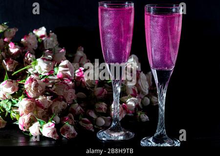 Strahlend brillantes Himbeer-Getränk. Sekt in zwei Gläsern steht auf einem Holztisch mit Eis. Für Blumen und eine Girlande. Kopierbereich Stockfoto