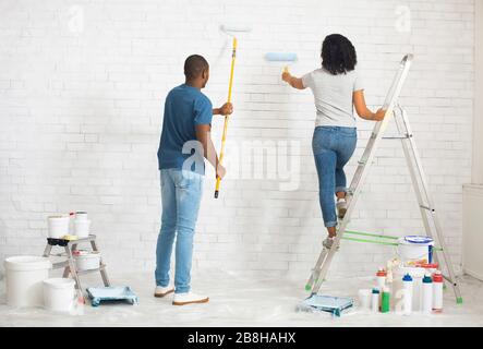 Mädchen auf Stepladder und Kerl malt Wand mit Rolle Stockfoto