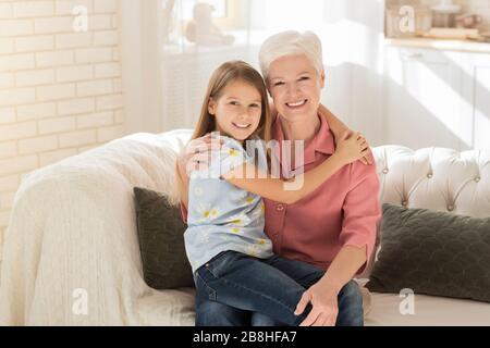 Freundschaft zwischen den Generationen. Süßes Kind mit ihrer Granny, die sich in einem sonnenbeleuchteten Zimmer umarmt Stockfoto