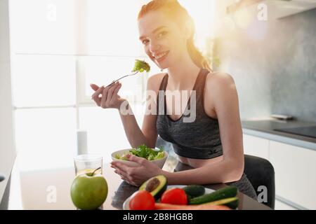Sportliches Mädchen mit Turnhallenkleidung isst Salat in der Küche Stockfoto