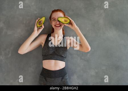 Sportliches Mädchen mit Turnhallenkleidung isst zu Hause Avocado Stockfoto