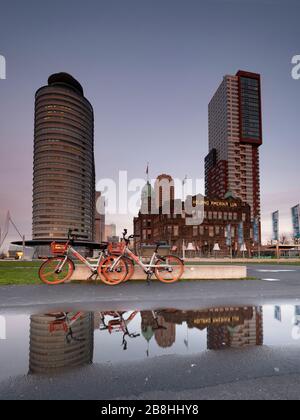 Rotterdam - 12. Februar 2019: Rotterdam, Niederlande. Hotel New York. Zwei rote Fahrräder, die vor dem Hotel geparkt wurden, das Hotel und die Fahrräder sind wieder da Stockfoto