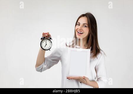 Schöne lächelnde Frau mit Wecker und leerem Brett für Text auf grauem Hintergrund. Beeilen Sie sich, etwas zu bestellen Stockfoto