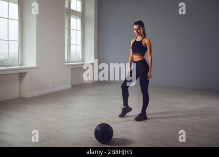 Das Mädchen geht mit einem medizinischen Ball in den Sport. Ein Sportmädchen übt Übungen in einem Raum im Haus aus. Stockfoto