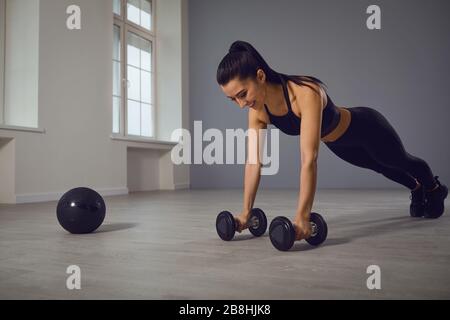 Sportliches Mädchen in schwarzer Sportswear, das in einem Raum drinnen Push-Up-Übungen macht. Stockfoto