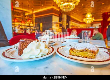 WIEN, ÖSTERREICH - 19. FEBRUAR 2019: Köstlicher Schokoladensacher-Kuchen (Sachertorte) und apfelstrudel mit Schlagsahne im prächtigen Sacher-Café -popul Stockfoto