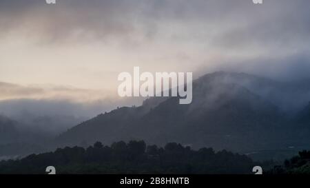 Ein entfernter Hügel, der von Nebel und niedrigen Wolken bedeckt ist Stockfoto