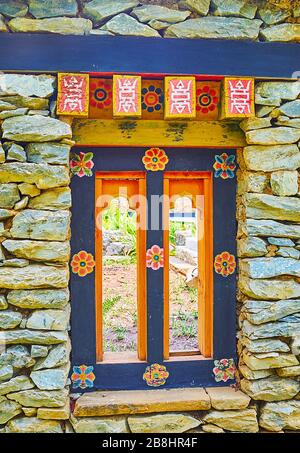 Die Nahaufnahme der Steinmauer und des kleinen Holzfensters, dekoriert mit primitiven Blumenmustern, Bauelementen im bhutanischen Garten, Rajapruek Par Stockfoto