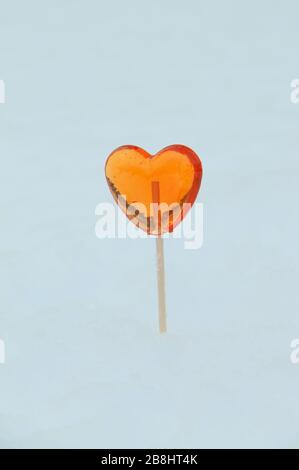 Roter, herzförmiger Lollipop sticht im Winter aus dem Schnee. Stockfoto