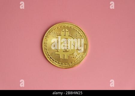 Goldmünze mit dem Bild von Bitcoin liegt auf einem rosafarbenen Hintergrund. Stockfoto