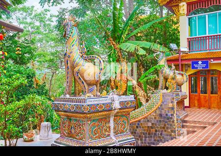CHIANG Mai, THAILAND - 7. MAI 2019: Verzierte Statuen von Singha-Löwen, bewachender Tempel, sind mit Tilling, Spiegelmosaik und feinem Blumenmuster dekoriert Stockfoto