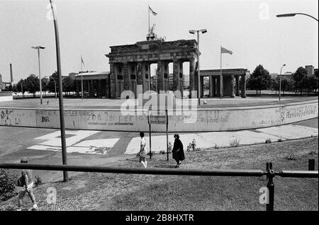 Menschen, die an einem Abschnitt der Berliner Mauer am Brandenburger Tor vorbeilaufen, von der westlichen Seite der Kluft aus gesehen. Die Berliner Mauer war eine von der Deutschen Demokratischen Republik (DDR, Ostdeutschland) am 13. August 1961 errichtete Barriere, die West-Berlin von der umliegenden DDR und von Ost-Berlin völlig abgrenzte. Die Mauer wurde am 9. November 1989 die freie Personenbewegung von Ost nach West erlaubt. Stockfoto