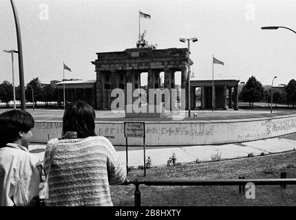 Menschen auf einer Aussichtsplattform, die von der westlichen Seite der Kluft aus auf einen Abschnitt der Berliner Mauer am Brandenburger Tor blickt. Die Berliner Mauer war eine von der Deutschen Demokratischen Republik (DDR, Ostdeutschland) am 13. August 1961 errichtete Barriere, die West-Berlin von der umliegenden DDR und von Ost-Berlin völlig abgrenzte. Die Mauer wurde am 9. November 1989 die freie Personenbewegung von Ost nach West erlaubt. Stockfoto