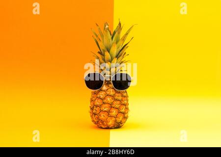 Ananas mit Sonnenbrille auf orangefarbenem und gelbem Hintergrund Stockfoto