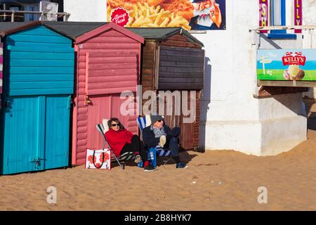 Ein Paar bietet Schutz vor dem kalten Wind und nutzt einen sonnigen Tag während der Pandemie von Covid 19, Broadstairs, Kent, Großbritannien Stockfoto