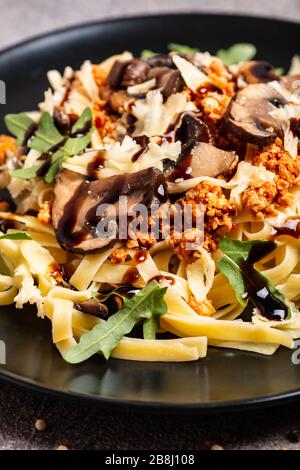 Bolognese Pasta mit Pilzen und Arugula auf schwarzem Teller gebuste Balsamico-Sauce. Draufsicht. Makro. Stockfoto