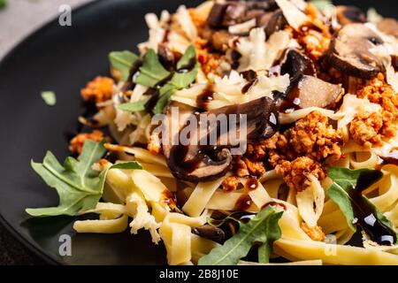 Bolognese Pasta mit Pilzen und Arugula auf schwarzem Teller gebuste Balsamico-Sauce. Draufsicht. Makro. Stockfoto