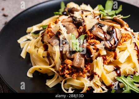 Bolognese Pasta mit Pilzen und Arugula auf schwarzem Teller gebuste Balsamico-Sauce. Nahaufnahme. Stockfoto