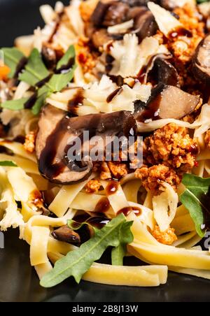 Bolognese Pasta mit Pilzen und Arugula auf schwarzem Teller gebuste Balsamico-Sauce. Draufsicht. Makro. Stockfoto