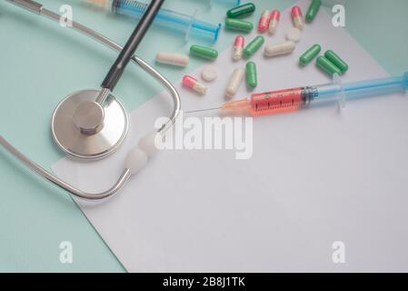 Eine Spritze mit einem Bluttest und ein Stethophonendoskop mit Ein Patientenfragebogen und Tabletten für eine Pandemie eines Cornovirus Stockfoto