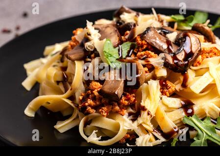 Bolognese Pasta mit Pilzen und Arugula auf schwarzem Teller gebuste Balsamico-Sauce. Stockfoto