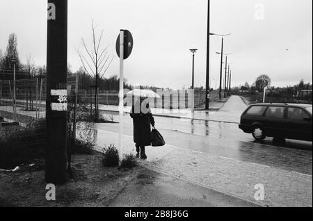 Eine Frau mit einem Regenschirm, der einen Fußgängerbereich des Verlaufs der ehemaligen Berliner Mauer, Südwest-Berlin, durchquert. Die Berliner Mauer war eine von der Deutschen Demokratischen Republik (DDR, Ostdeutschland) am 13. August 1961 errichtete Barriere, die West-Berlin von der umliegenden DDR und von Ost-Berlin völlig abgrenzte. Die Mauer wurde am 9. November 1989 die freie Personenbewegung von Ost nach West erlaubt. Stockfoto