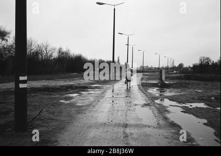 Ein Mann, der auf einem Fußgängerüberweg über den Verlauf der ehemaligen Berliner Mauer im Südwesten Berlins spaziert. Die Berliner Mauer war eine von der Deutschen Demokratischen Republik (DDR, Ostdeutschland) am 13. August 1961 errichtete Barriere, die West-Berlin von der umliegenden DDR und von Ost-Berlin völlig abgrenzte. Die Mauer wurde am 9. November 1989 die freie Personenbewegung von Ost nach West erlaubt. Stockfoto