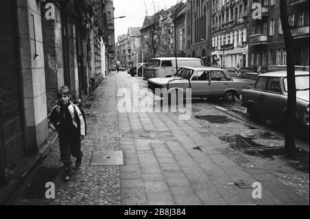 Ein Junge, der an einem Straßenbelag vorbei an einem verlassenen Lada-Auto, Prenzlauer Berg, Berlin, spazieren geht. Die Berliner Mauer war eine von der Deutschen Demokratischen Republik (DDR, Ostdeutschland) am 13. August 1961 errichtete Barriere, die West-Berlin von der umliegenden DDR und von Ost-Berlin völlig abgrenzte. Die Mauer wurde am 9. November 1989 die freie Personenbewegung von Ost nach West erlaubt. Stockfoto