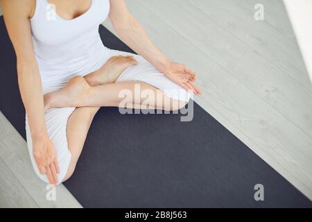 Yoga-Frau in weißer Kleidung meditiert im Raum ruhig sitzend in lotus-position. Stockfoto