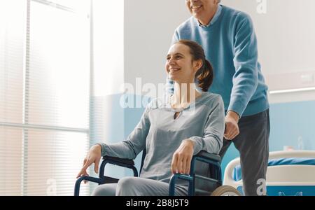 Vater, der ihre Tochter im Rollstuhl im Krankenhaus, in der Familie und im Gesundheitskonzept unterstützt Stockfoto