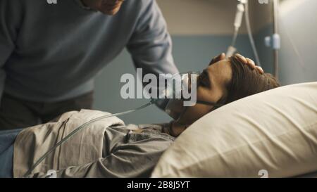 Pflegender leitender Vater, der die Tochter unterstützt, die mit einer Sauerstoffmaske in einem Krankenhausbett liegt, berührt er ihren Kopf Stockfoto