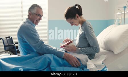 Vater, der ihre Tochter im Krankenhaus besucht, bringt ihr ein schönes Geschenk Stockfoto