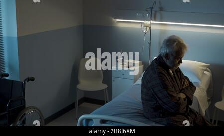 Depressiver älterer Mann sitzt nachts allein auf dem Krankenbett, er fühlt sich einsam und traurig Stockfoto