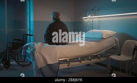 Depressiver älterer Mann sitzt nachts allein auf dem Krankenbett, er fühlt sich einsam und verlassen Stockfoto