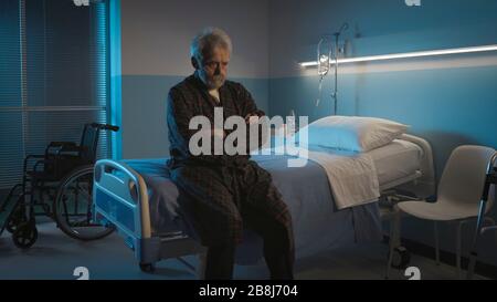 Depressiver älterer Mann sitzt nachts allein auf dem Krankenbett, er fühlt sich einsam und verlassen Stockfoto