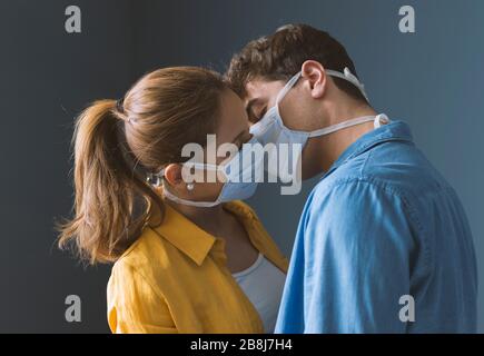 Junge Millennials Paar, die schützende Gesichtsmasken tragen und sich küssen, Virus-Spread-Prävention und das Konzept der Menschen Stockfoto